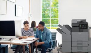 Oficina moderna con empleados trabajando en equipo junto a una impresora multifunción Sharp BP-50C36 A3 Color.